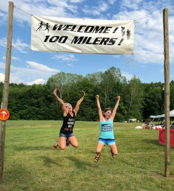 Two women jumping in the air in front of a welcome sign.