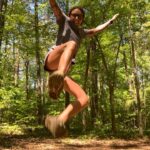 A woman jumping in the air in the woods.